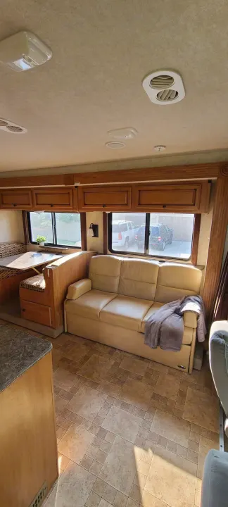 Bright RV rental living space with a comfortable light-colored sofa, dinette booth, and ample wooden cabinets.. Jamboree Jamboree Motorhome 2011