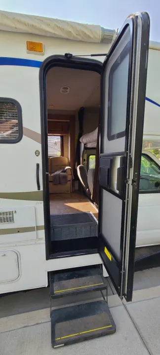 Open RV door with extended steps, showing the inviting interior with a recliner, bunk, and wood floor. Ideal for an RV rental.. Jamboree Jamboree Motorhome 2011