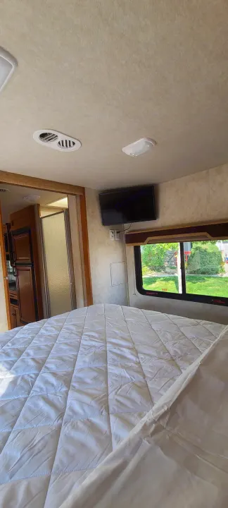 Cozy RV rental bedroom: Quilted bed, wall-mounted TV, window with outdoor view, and adjacent compact living space.. Jamboree Jamboree Motorhome 2011