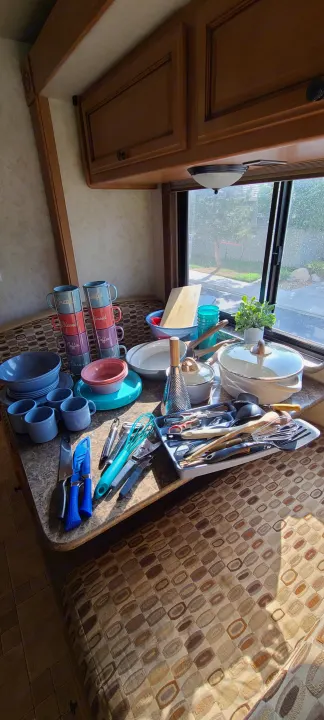 A fully stocked kitchen setup in an RV rental, featuring new dishes, cookware, and utensils on a sunlit counter.. Jamboree Jamboree Motorhome 2011