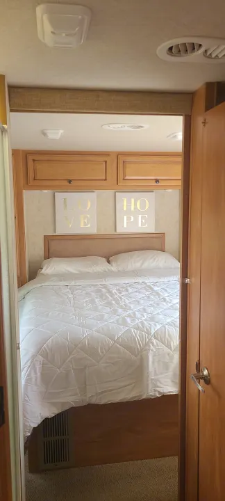 RV rental bedroom features a comfy bed with white bedding, "LOVE" and "HOPE" signs, cabinets, and ceiling vents.. Jamboree Jamboree Motorhome 2011