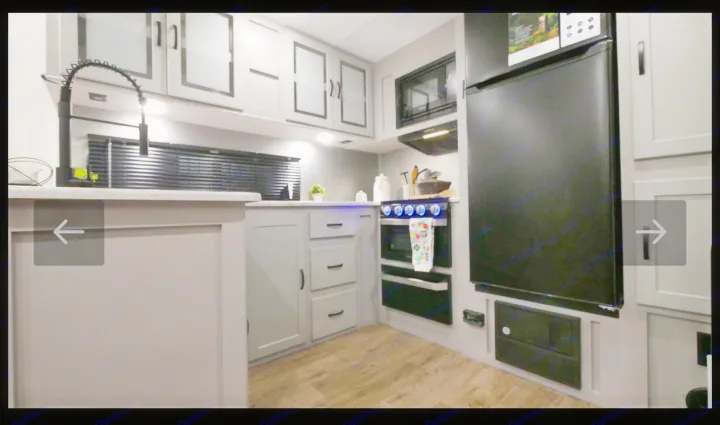Modern RV rental kitchen: light gray cabinets, black appliances, sink, stove, fridge, wood-look floor. Compact design.. Forest River Vibe Travel Trailer 2022
