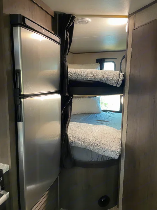 Inside an RV rental: two cozy bunk beds with soft bedding, a shiny stainless steel refrigerator, and windows.. Jayco Jay Flight SLX 2021