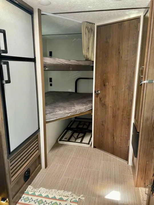 RV rental interior features bunk beds, a refrigerator, and a wood-grain door. Ideal for family adventures.. Keystone RV Passport SL 2020