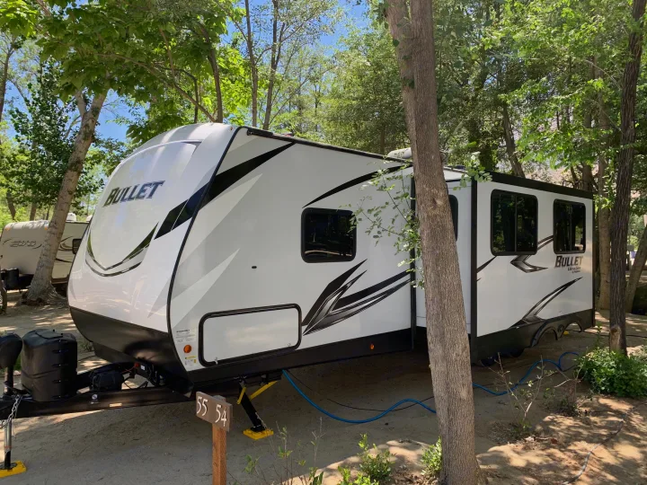 White Bullet RV rental parked at a shaded campsite, ready for adventure. Ideal for outdoor camping and travel.. Keystone Bullet 2021