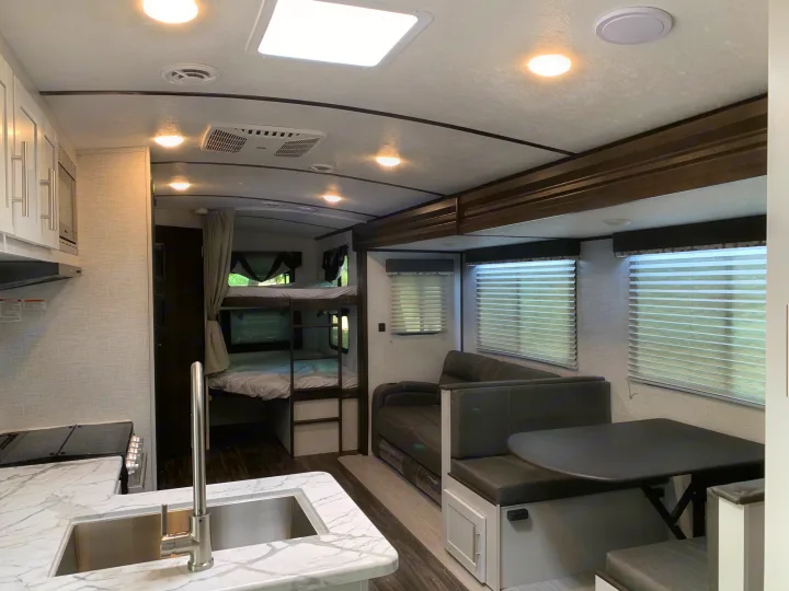 Spacious RV rental interior featuring a modern kitchen with sink, dining booth, and bunk beds for comfortable travel.. Keystone Bullet 2021