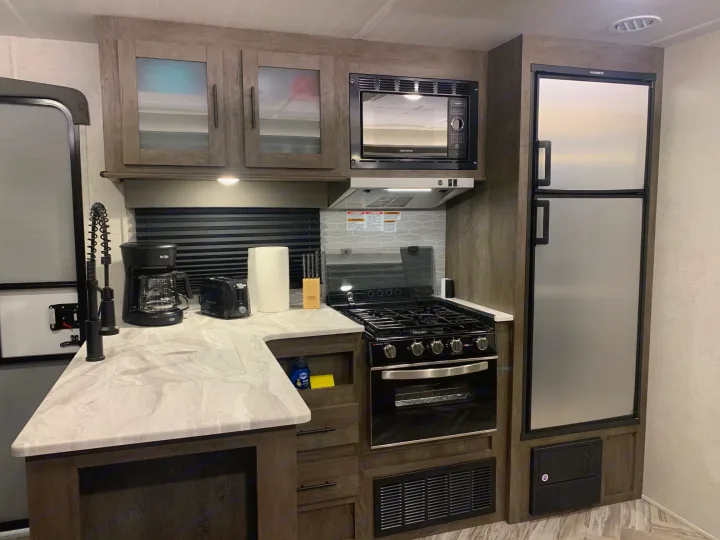 Modern RV rental kitchen interior: microwave, stove, oven, sink, and large refrigerator. Ready for your trip!. Forest River Wildwood 2021