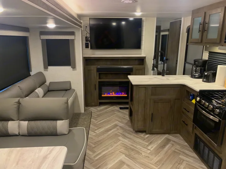 Explore this inviting rv rental interior! Features a modern living area with sectional sofa, cozy fireplace, and fully equipped kitchen.. Forest River Wildwood 2021