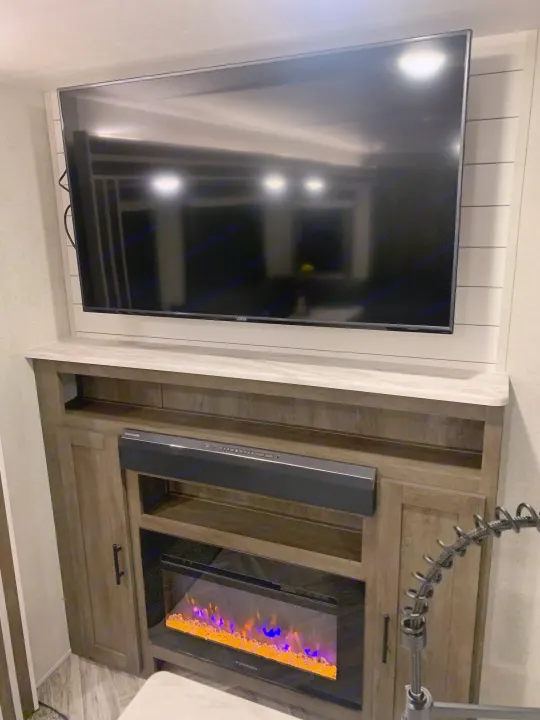 Modern RV rental interior: Flat-screen TV, electric fireplace, and soundbar in a cozy living area.. Forest River Wildwood 2021