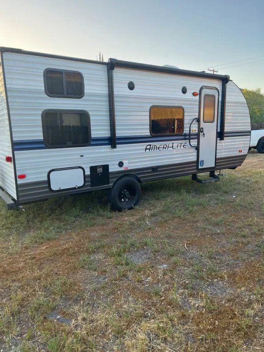 Grey & white Ameri-Lite travel trailer, perfect for your next RV rental. Parked outdoors on dry grass.. Travel Lite Superlite 2022