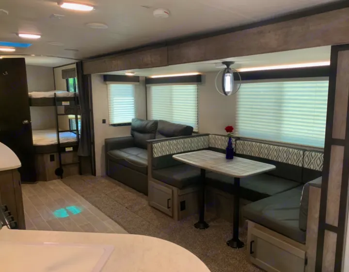 Experience this RV rental's cozy interior: bunk beds, a dark sofa, and a U-shaped dinette with a table and red rose.. Heartland Wilderness 2020