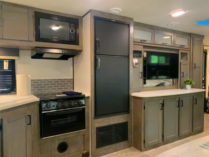 Inside a modern RV rental: a well-equipped kitchen with microwave, stove, and fridge, plus a living area with TV.. Heartland Wilderness 2020