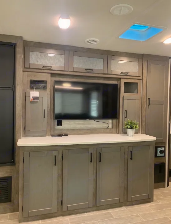 Inside an RV rental: sleek entertainment unit with TV, ample grey cabinets, and bright ambient lighting for a modern living space.. Heartland Wilderness 2020
