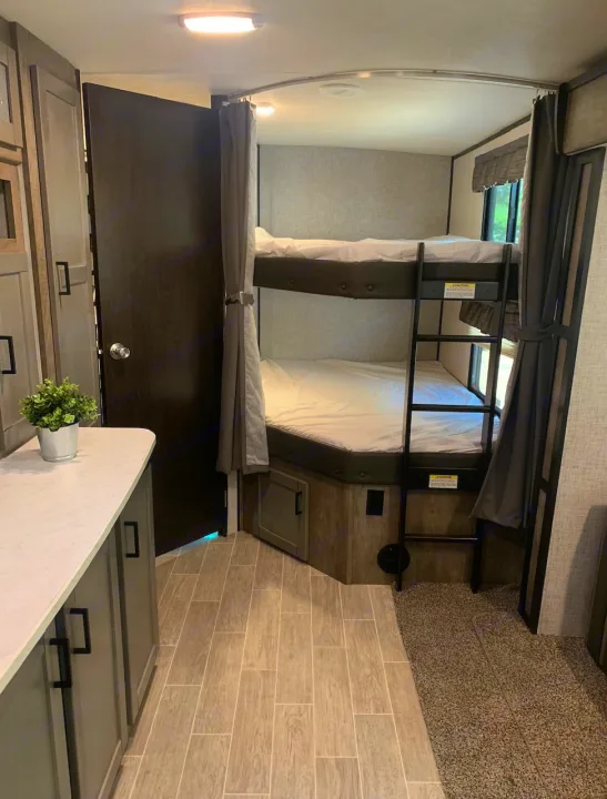 RV rental's interior: comfy bunk beds with ladder, privacy curtains, and a compact living area with diverse flooring.. Heartland Wilderness 2020
