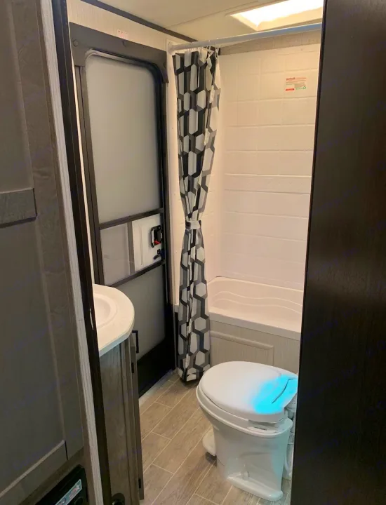This RV rental bathroom features a compact sink, toilet, and shower with a geometric curtain, optimized for travel comfort.. Heartland Wilderness 2020