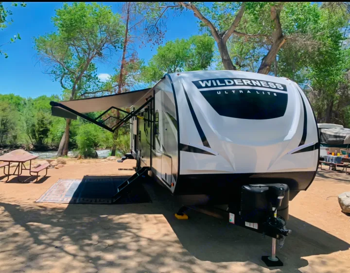 Wilderness Ultra-Lite RV rental at a riverside campsite with extended awning and picnic table for outdoor enjoyment.. Heartland Wilderness 2020
