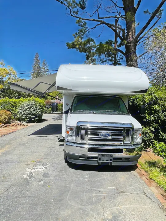 White Ford RV rental with awning extended, parked on a sunny paved driveway amidst greenery.. Jayco Redhawk 2021