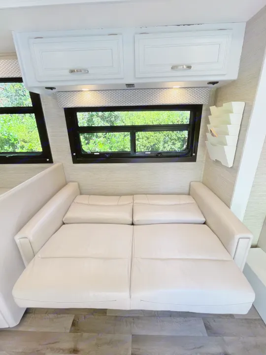 Relax in this RV rental's extended sofa, offering comfortable sleeping. Overhead cabinets and bright windows complete the cozy interior.. Jayco Redhawk 2021