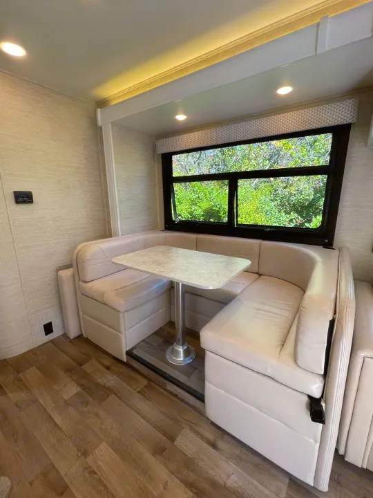 Spacious RV rental dinette with U-shaped booth seating, light table, and large window showcasing nature. Perfect for meals on the go.. Jayco Redhawk 2021