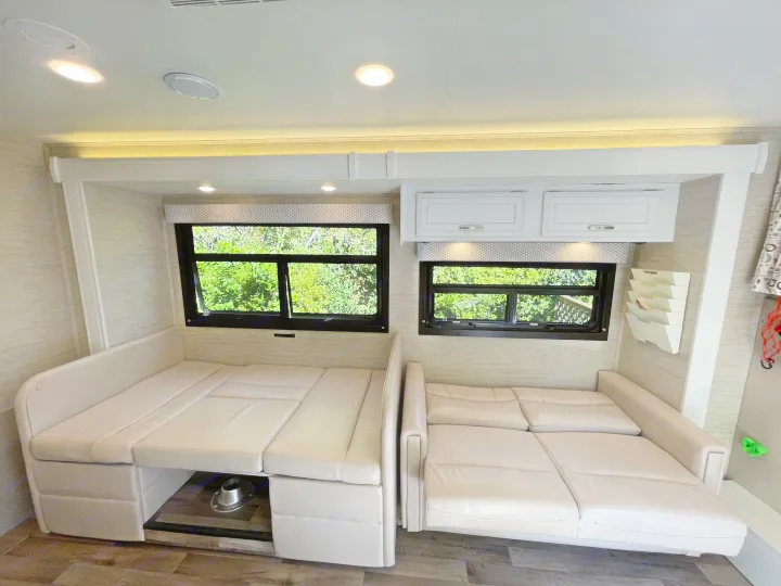 Bright, modern RV rental interior featuring convertible dinette and sofa seating with nature views. Cozy and functional.. Jayco Redhawk 2021