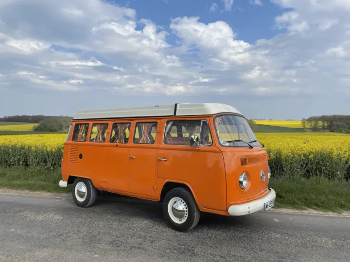 Vibrant orange vintage VW camper van by yellow rapeseed field. Your perfect RV rental for a scenic escape!. Volkswagen westfalia 1984