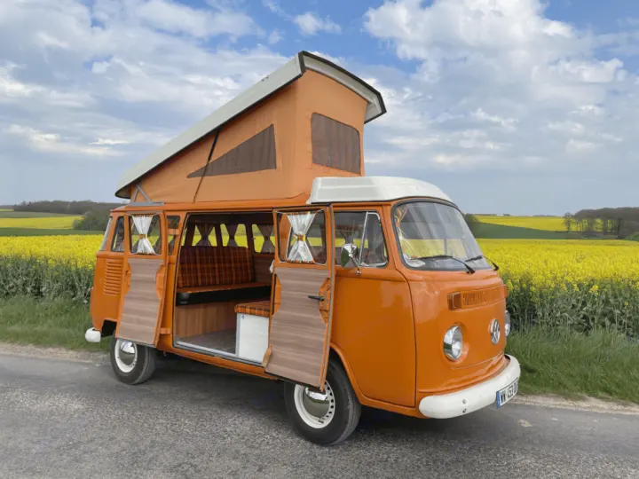 Experience adventure! This orange vintage VW camper van, ideal for RV rental, is parked amidst vibrant yellow fields.. Volkswagen westfalia 1984