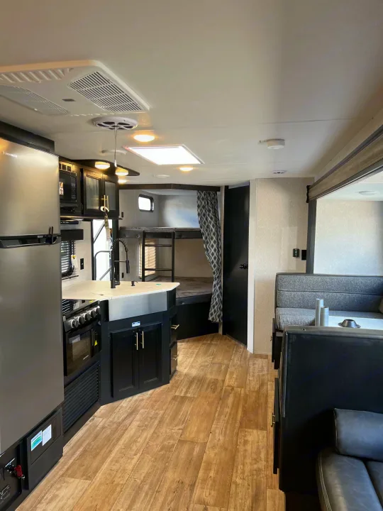 This rv rental interior features a full kitchen, dining booth, and private bunk bed area, designed for travel comfort.. Forest River Cherokee Grey Wolf 2022