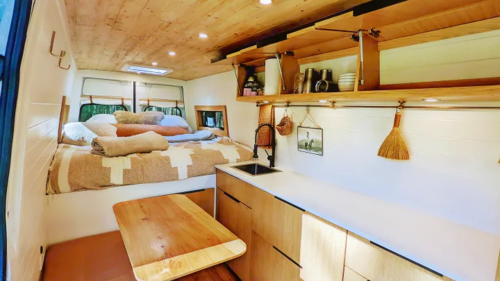 Inside a spacious RV rental: a cozy bedroom, well-equipped kitchen with sink, fold-down table, & ample storage.. Mercedes-Benz Sprinter 2020