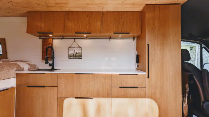 This RV rental showcases a bright, modern interior with natural wood cabinets, a compact kitchen sink, and cozy bed area.. Mercedes-Benz Sprinter 2020