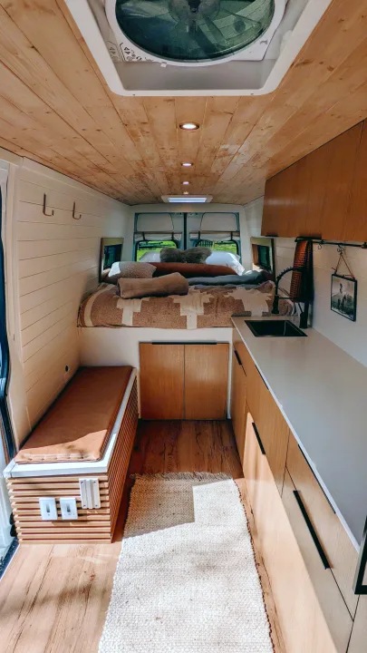 Cozy rv rental interior featuring a wood ceiling, shiplap walls, compact kitchen, and a comfy bed. Perfect for van life adventures!. Mercedes-Benz Sprinter 2020