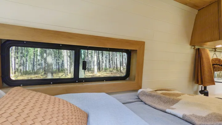 Cozy rv rental bedroom: a bed with pillows faces a window with a sunlit forest view. White shiplap walls & wood trim.. Mercedes-Benz Sprinter 2020