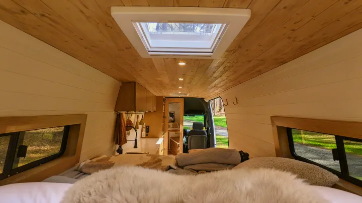 Cozy rv rental interior: view from the bed with fluffy blankets, showcasing a wood ceiling, skylight, and galley kitchen.. Mercedes-Benz Sprinter 2020
