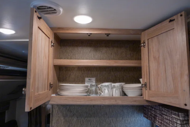 Open RV rental cabinet stocked with plates, bowls, glasses, & mugs. Roadside assistance info visible inside.. Forest River Sunseeker LE 2017