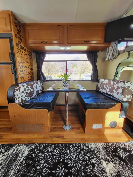 Inviting RV rental dinette: cozy black & cow print seating, wooden cabinets, and a table set for four with scenic views.. Thor Majestic 2014