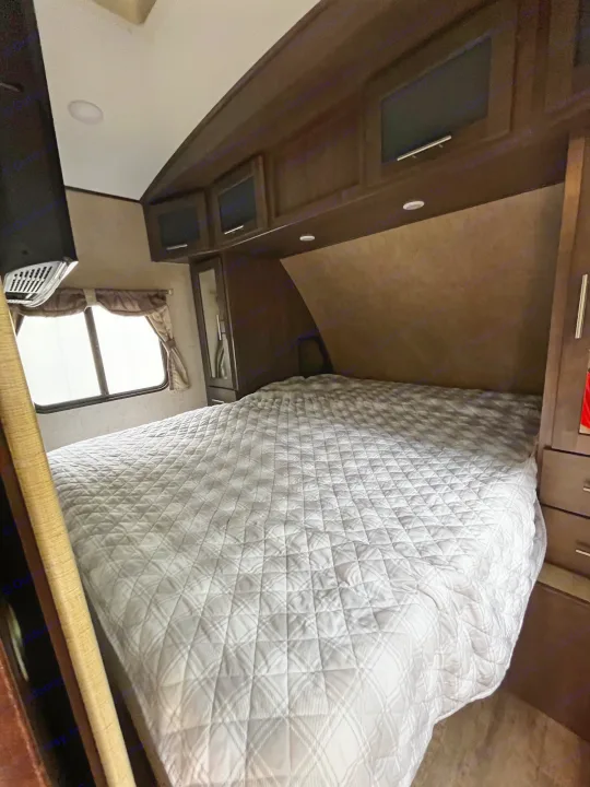 Cozy RV rental bedroom featuring a comfy bed, overhead storage, and a window. Perfect for your next adventure!. Forest River Surveyor 2015