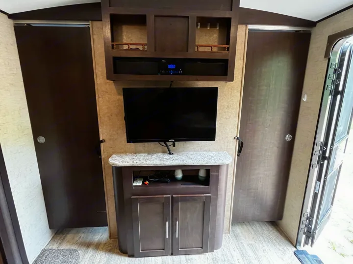 RV rental interior: Entertainment area featuring a TV, soundbar, and storage cabinet, flanked by two dark brown sliding doors.. Forest River Surveyor 2015
