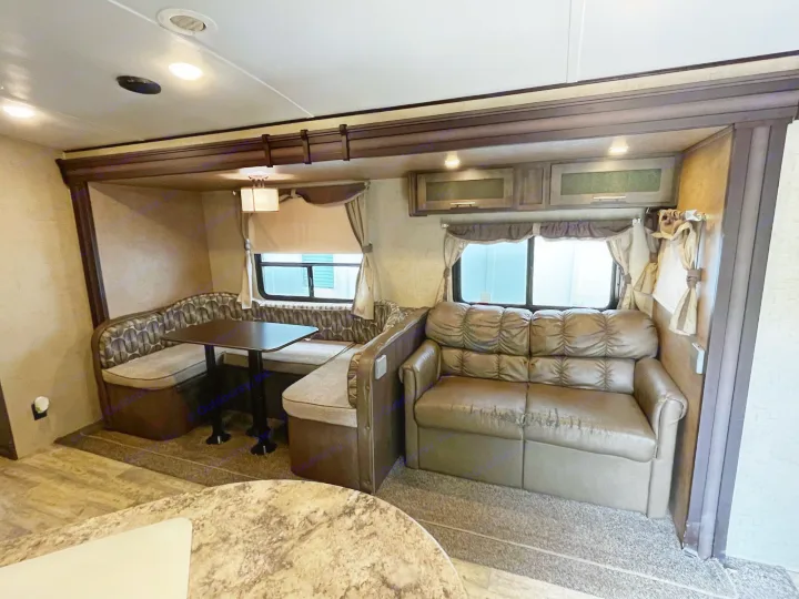 Cozy RV rental interior featuring a dining booth, table, and a comfortable sofa with overhead storage.. Forest River Surveyor 2015