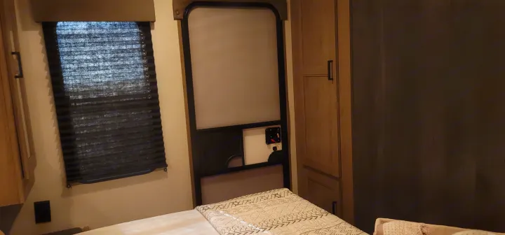 Cozy RV rental bedroom with a striped bed, shaded window, narrow door, and light wood cabinets for storage.. Keystone RV Hideout Luxury Edition 2021