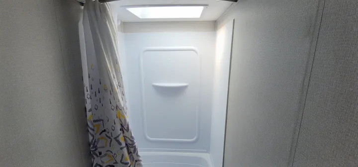 RV rental bathroom: Clean, compact shower with a bright white stall, small shelf, and geometric patterned curtain.. Keystone RV Hideout Luxury Edition 2021