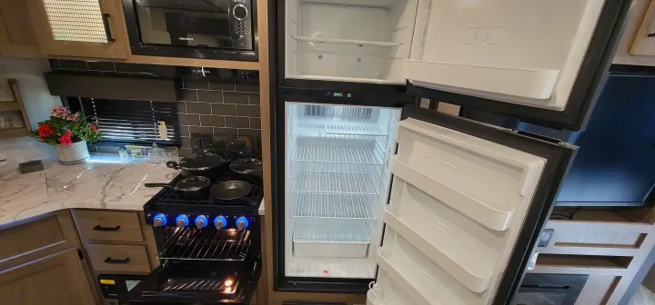RV rental kitchen featuring an open, empty fridge, stove with open oven, microwave, and ample counter space.. Keystone RV Hideout Luxury Edition 2021