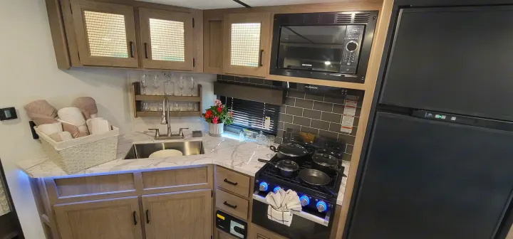 Bright, modern RV rental kitchen with a sink, microwave, stove, and large refrigerator.. Keystone RV Hideout Luxury Edition 2021