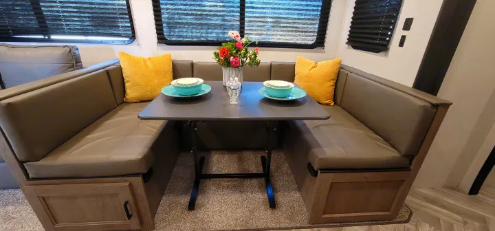 RV rental's cozy dinette: U-shaped seating with yellow pillows, table set with teal dishes, and flowers.. Keystone RV Hideout Luxury Edition 2021