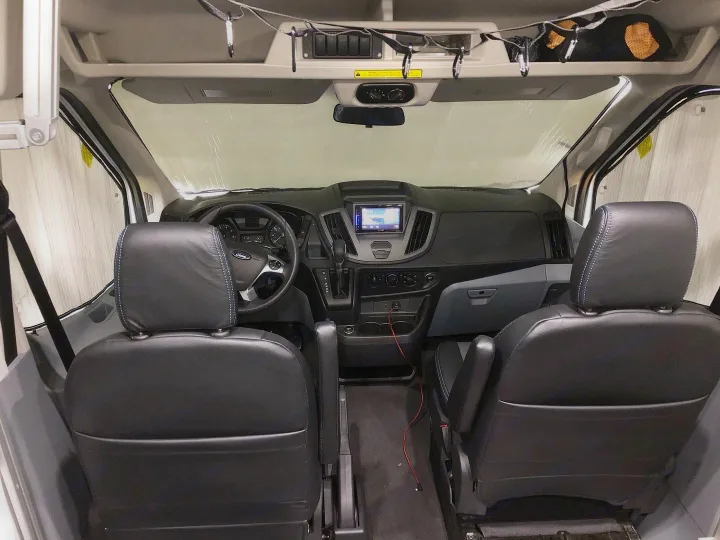 Spacious RV rental van interior, showing two dark front seats, the dashboard, and a sunshade on the windshield.. vandoit DO 2018