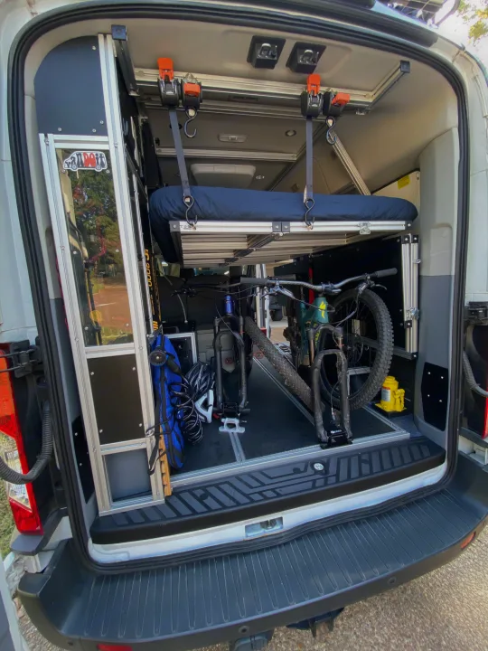 Inside an RV rental: custom camper van interior with elevated bed and two mountain bikes secured for travel.. vandoit DO 2018