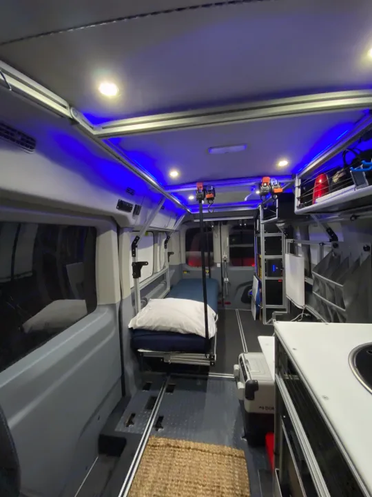 Spacious RV rental interior with a bed, bright and blue ambient lighting, kitchen, and versatile track floor.. vandoit DO 2018