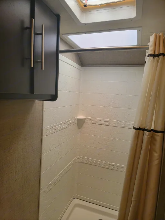 RV rental bathroom: functional shower space with textured white walls, cream curtain, and dark cabinet.. Thor Axis 2021
