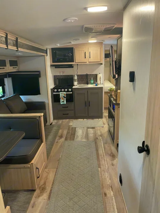Modern RV rental interior showing a comfortable living/dining area, full kitchen, and compact bedroom in light wood & gray.. Heartland Sundance 294BH 2022