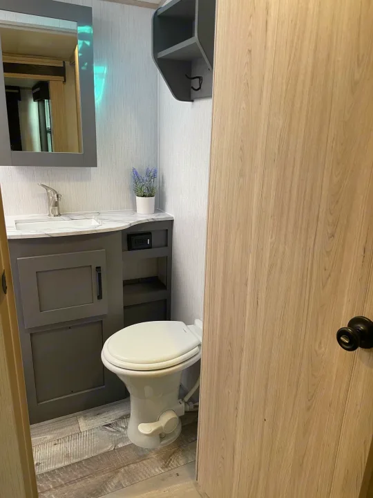 This rv rental features a compact bathroom with a sink, mirror, toilet, and light wood-look finishes.. Heartland Sundance 294BH 2022