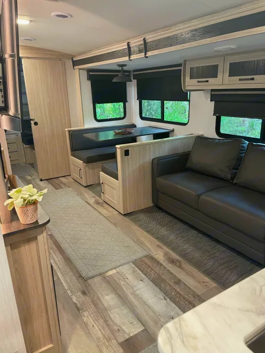 This modern rv rental boasts a comfortable gray sofa, dinette with seating, and light wood interior.. Heartland Sundance 294BH 2022