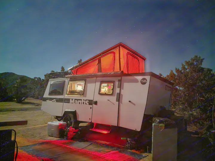 **RV rental** camper trailer at night, glowing red under a starry sky. Ideal for a memorable outdoor adventure.. TAXA Habitat Mantis 2021